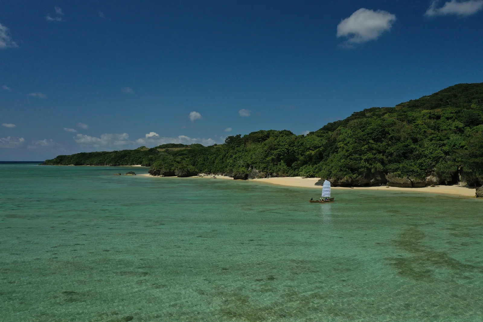 A sailboat beside a sandy cove and wooded coast on Ishigaki