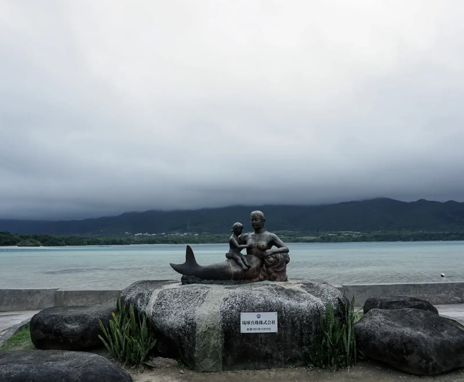 Low clouds hanging over the mountains at Kabira Bay, with the pearl statue in the foreground