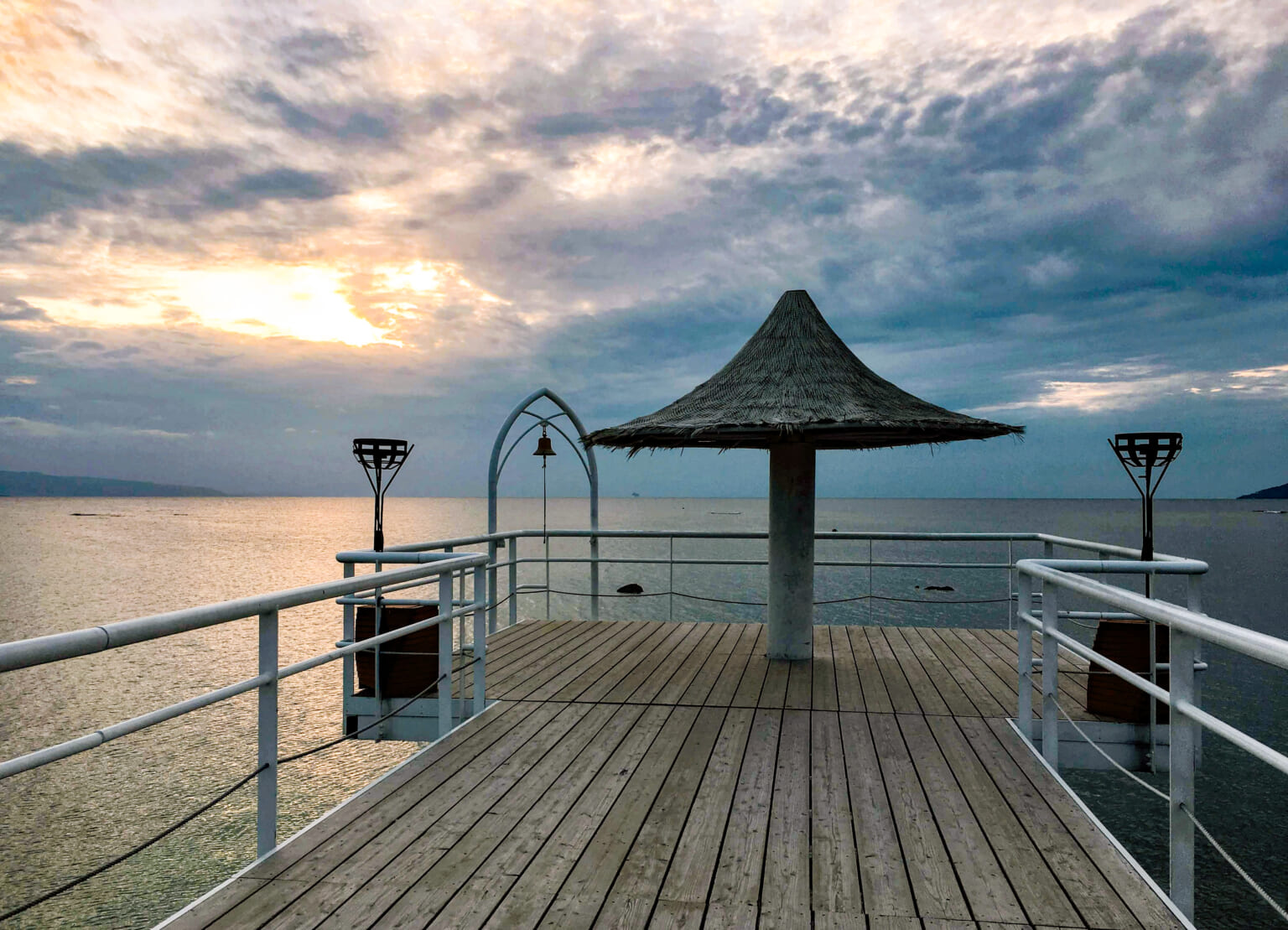 The wooden pier at Fusaki, with a thatched shelter and sunset over the sea.