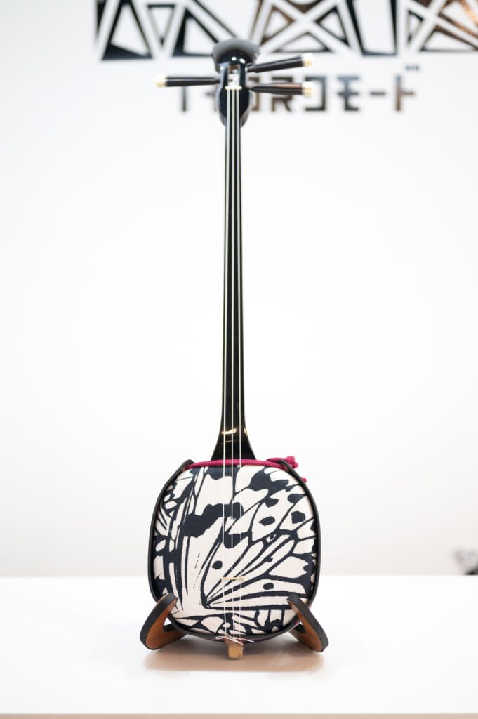 Original black and white three stringed Okinawa music instrument Sanshin with screen printed Oogomadara design from designer Yasutake Ikeshiro. Each Sanshin's note carries the islands’ soul, echoing a rich musical heritage kept alive in every folk song.