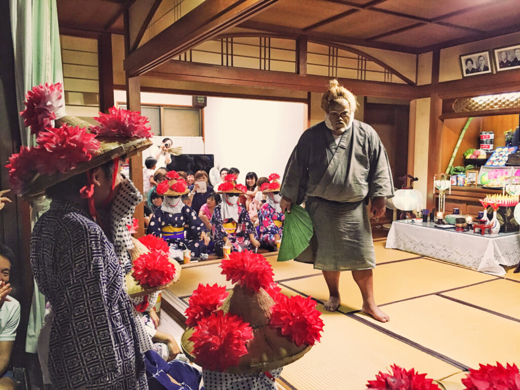 Angama masked villagers visit homes during Obon, blending humor, song, and ancestor respect.